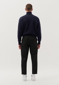Granatowy sweter z wysokim kołnierzem, w połączeniu z czarnymi spodniami o dopasowanym kroju. Białe sneakersy, widoczne przeszycia na spodniach, minimalistyczny design.
