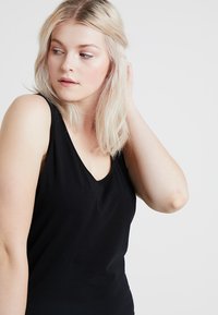 Fekete ujjatlan felső V-dekoltázzsal, puha anyagból és kirúzott szabású. Simaszerű textúra minimális varratokkal és díszítésekkel.