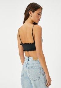 Zwart cropped top met gerimpelde randen, dunne verstelbare bandjes, gecombineerd met lichtblauwe high-waisted jeans met achterzakken en een label.