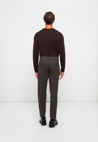 Brown long-sleeve shirt paired with grey tailored trousers. Black shoes complete the look, showcasing a simple yet modern design.