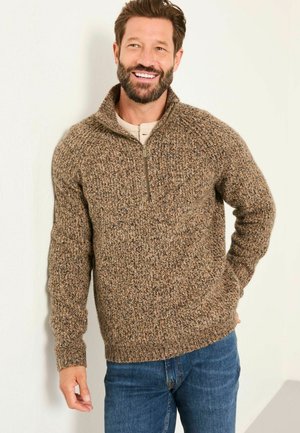 Brauner, strukturierter Pullover mit Reißverschluss und dickem Strickdesign, mit gerippten Bündchen und Saum, getragen über einem hellen Hemd und kombiniert mit blauen Jeans.