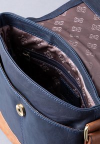 Navy leather bag with a light brown bottom, featuring a gold snap closure and a patterned brown interior with a zippered pocket.