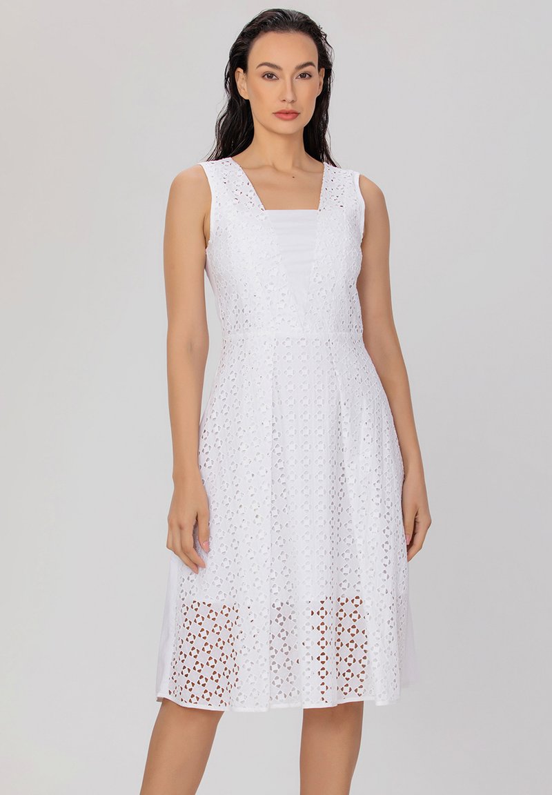 Robe blanche avec des motifs circulaires découpés au laser, un corps ajusté et une jupe évasée, avec un décolleté carré et sans manches.