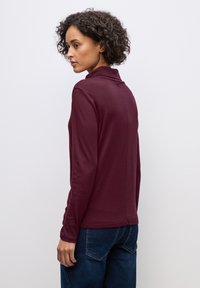 Bordeaux langemouwtop met een nekkraag en een gladde textuur, met een getailleerd ontwerp en subtiele naaddetails aan de achterkant.