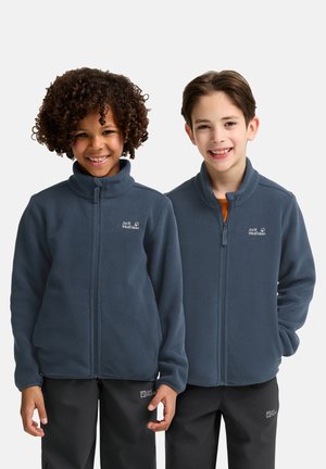 Deux enfants portant des vestes en polaire bleues avec des cols hauts et des zips, arborant un logo sur la poitrine gauche et accompagnées de pantalons noirs.