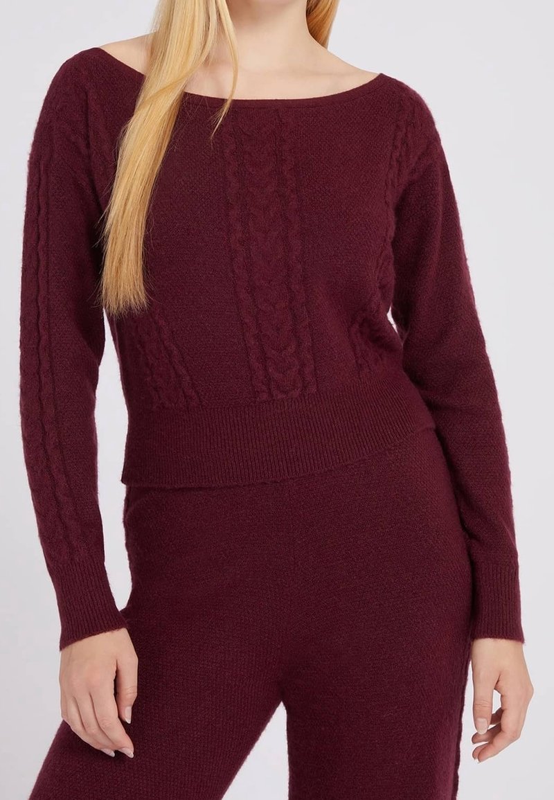Femme portant un ensemble pull et pantalon en maille violet foncé avec des détails torsadés sur les manches et le devant.