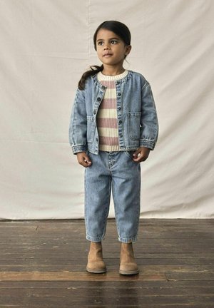 Giacca di jeans con chiusura a bottoni e tasche laterali, maglione a righe in maglia, pantaloni di jeans a sigaretta e stivali beige alla caviglia. Sfondo in legno chiaro.