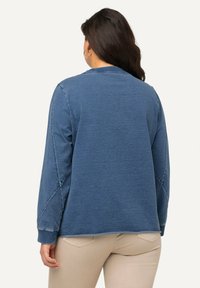 Modrý pulover s dlouhými rukávy, kulatým výstřihem a postranními švy. Měkká textura, uvolněný střih a šití na rukávech.