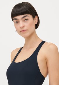 Maillot de bain bleu marine avec un décolleté rond et des bretelles fines, fabriqué dans un matériau lisse et extensible. Présente un design ajusté avec des coutures minimales.