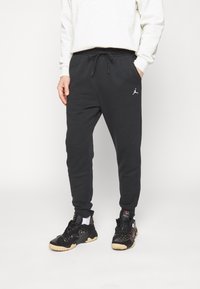 Černé tepláky s elastickým páskem a šňůrkou; mají bílou Jordan logo na levém stehně; spárování s černými sportovními botami.