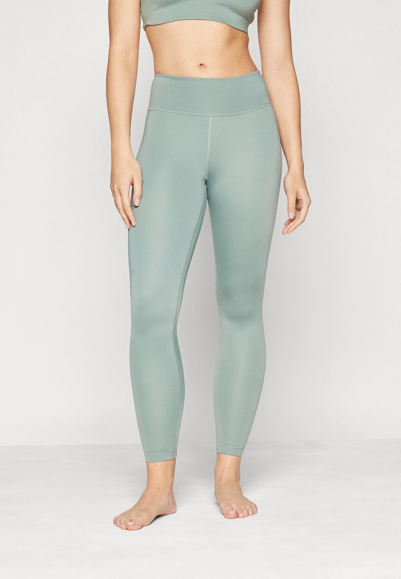 Legging vert clair en matériau extensible avec une taille haute, design ajusté et texture lisse et mate. Aucun motif ou accessoire visible.
