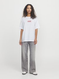Hvit oversized t-skjorte med rød tekst som sier "LOVER NOT A FIGHTER," kombinert med falmede grå vid benbukser og grå joggesko.