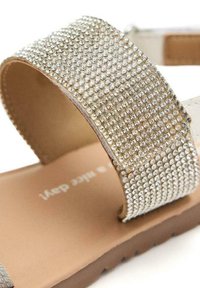 Sandalo d'oro con una ampia cinturino decorato con strass trasparenti, una soletta beige liscia e una suola marrone resistente con presa testurizzata.