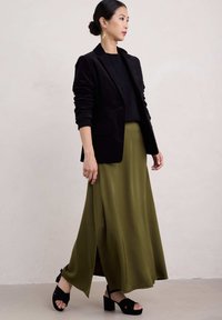 Černý sametový blejzr, černý pletený top, splývavá sukně olivové barvy s bočním rozparkem a černé sandály na blokovém podpatku. Zlaté náušnice dodávají detail.