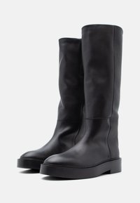 Czarne skórzane kozaki za kolano o zaokrąglonym nosku, z masywną podeszwą na platformie i gładką fakturą. Minimalistyczny design bez widocznych elementów metalowych.