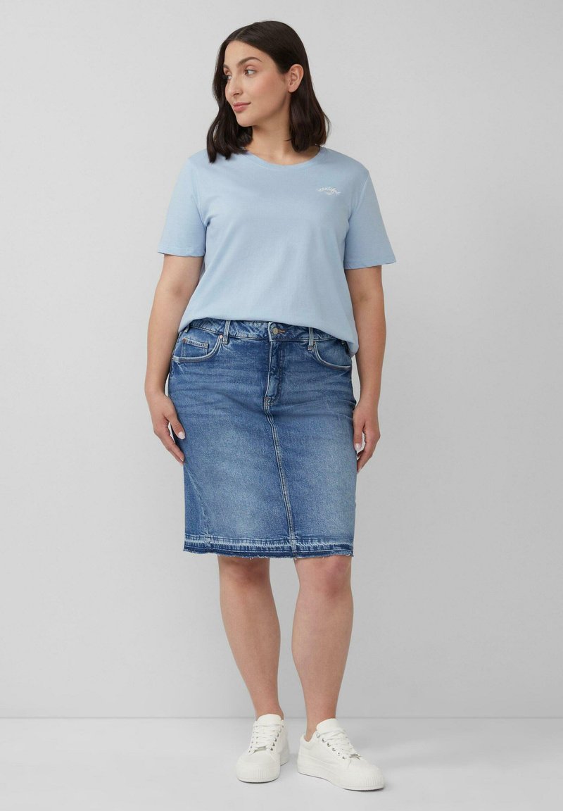 Helles blaues Baumwoll-T-Shirt mit kurzen Ärmeln und weißem Logo, kombiniert mit einem knielangen Jeansrock. Weiße Sneaker runden den Look ab.