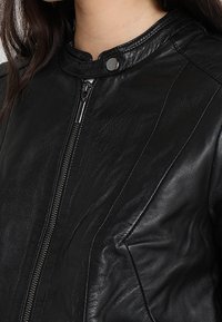 Černá kožená bunda na zip s dekorativními švy a drukem na límci. Má texturovaný povrch, což jí dodává elegantní a moderní vzhled.