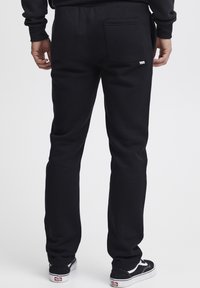 Black sweatpants with elastic waistband and back pocket, made of soft fabric. Paired with black Vans shoes featuring white accents.