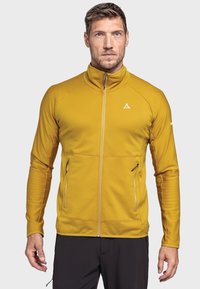 Gelbe Zipjacke mit langen Ärmeln, strukturiertem Stoff, zwei Fronttaschen und hohem Kragen. Markenlogo auf der Brust und am Ärmel.