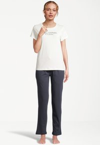 Ljusgrå t-shirt med svart text och mörkblå byxor. Outfiten har en enkel design och en avslappnad passform. Barfota, stående mot en neutral bakgrund.