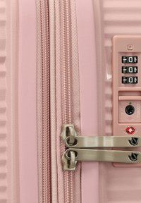 Valigia rigida rosa chiaro con superficie texturizzata, doppia cerniera e lucchetto con combinazione approvato dalla TSA sul lato.