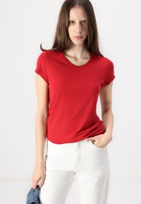 Röd kortärmad t-shirt i ett mjukt, lättviktsmaterial med rundad halsringning, parat med vita höga jeans. Med minimalistisk detaljer.