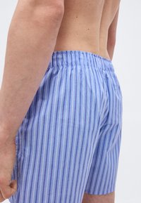 Gros plan sur une personne portant un boxer à rayures verticales bleu et blanc, montrant le dos et le côté du torse.