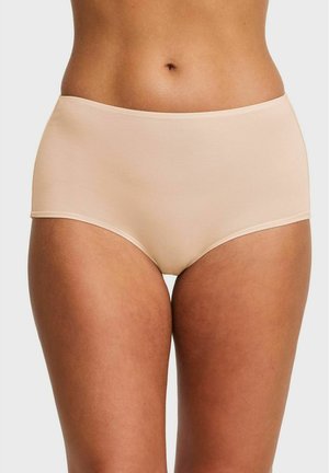 Vrouw draagt beige, naadloos katoenen ondergoed met hoge taille, getoond van taille tot midden bovenbeen tegen een effen achtergrond.