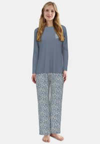 Grijs top met lange mouwen en een logo op de borst, en blauwe pyjamabroek met een patroon van abstracte witte ontwerpen. Zachte stof, comfortabele pasvorm.