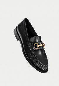 Schwarze Leder-Slipper mit runder Zehenform, geflochtenen Details und einer goldfarbenen Kettenakzentierung im oberen Bereich. Flache Sohle, glatte Oberfläche.