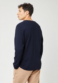 Camicia a maniche lunghe blu navy in tessuto a maglia testurizzata, con colletto rotondo e taglio rilassato, abbinata a pantaloni in corduroy color sabbia chiaro.