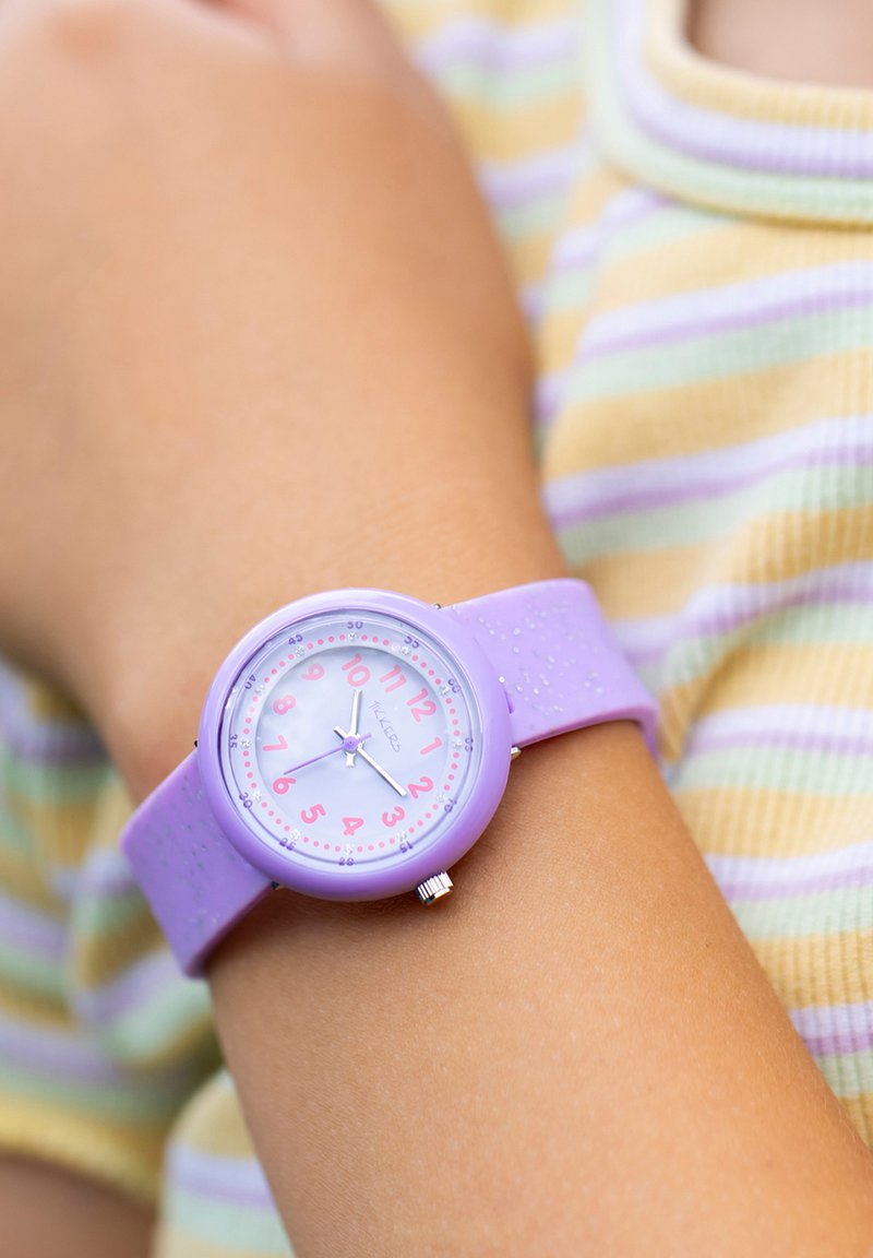 Montre violette avec un bracelet en silicone, chiffres roses sur un cadran violet clair, dotée d'un petit bouton argenté et d'un bracelet texturé.