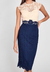 Krajková šaty s krémovým vrškem a námořnickou krajkovou tužkovou sukní se květinovými vzory a vroubkovaným lemem. Krátké rukávy a přiléhavý střih.