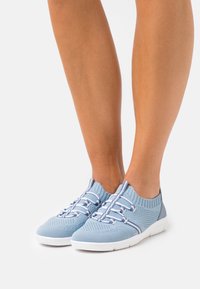 Ljusblå stickade sneakers med en andningsbar struktur, elastiska snören och en vit gummisula. Har en kontrasterande blå hälpanel.