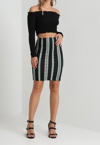 Černý crop top bez ramínek s nabíranou strukturou, zkombinovaný s černou a pruhovanou tužkovou sukní ke kolenům. Černé páskové sandály se cvočky.