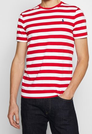Czerwono-biała koszulka z krótkim rękawem w paski, z okrągłym dekoltem i małym niebieskim logo na lewej piersi. Gładki bawełniany materiał.