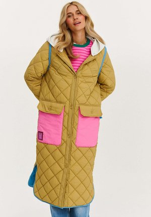 Pikowana długa kurtka w musztardowym kolorze z różowymi kieszeniami, kontrastowym niebieskim wykończeniem i kapturem. Posiada zapięcie na guziki oraz detal naszywki.