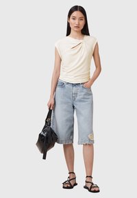 Crème gebreide top met een knoopdetail, gecombineerd met lichtblauwe versleten denim shorts. Een zwarte handtas en sandalen met banden maken de look compleet.