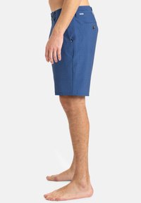 Modré nohavice vyrobené z textúrovanej tkaniny, s rovnomerným strihom, dvoma bočnými vreckami a gombíkovými detailmi na páse a zadných vreckách.