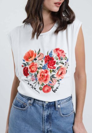 Donna che indossa un top bianco senza maniche con motivo floreale colorato a forma di cuore e testo "love" abbinato a jeans blu.