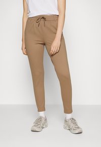 Tan tapered joggingbroeken met een trekkoord in de taille, gemaakt van zachte stof, voorzien van zijzakken en een gladde structuur. Gecombineerd met lichte sneakers.