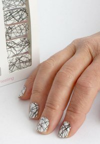 Nagelüberzüge mit weißem Grund und schwarzen abstrakten Linienmustern, präsentiert neben einer Hand vor einem hellen Hintergrund.