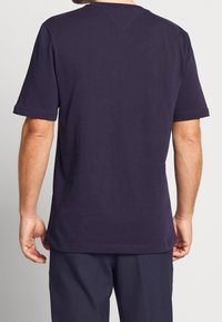 Námořnická modrá tričko s krátkým rukávem a klasickým kulatým výstřihem, hladká textura a šitý lem, s minimalistickým designem.