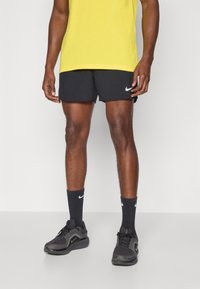 Musta urheilushortsit, joissa valkoinen Nike-logo, yhdistettynä mustiin sukkiin, joissa valkoinen Nike-logo, ja mustat juoksukengät, joissa on teksturoidut kuviot.