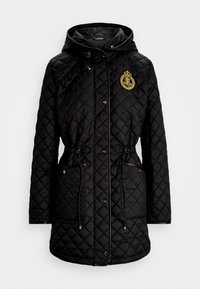 Svart kviltad jacka med huva, med en gyllene emblem, tryckknappar, dragsko i midjan och kontrasterande släta detaljer.