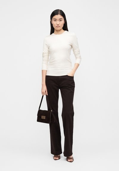 Haut crème côtelé à manches longues associé à un pantalon évasé marron foncé et un petit sac à main en daim marron avec une fermeture dorée.