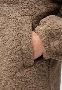 Bruine fleecejas met een gestructureerd oppervlak, voorzien van een zijzak en aansluitende manchetten, met een warm, zacht ontwerp.