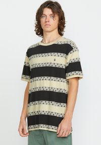 Kortermet t-shirt i beige, sort og mønstrede striber. Har et lille emblem på brystet og en løs pasform. Blødt bomuldsstof.