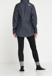 Wodoodporna szara kurtka męska z kapturem, regulowaną talią i logo na plecach. Do tego czarne spodnie i wysokie trampki.