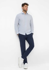 Lichtblauwe button-up shirt met kleine witte geometrische patronen, gecombineerd met marineblauwe broek en witte sneakers. Eenvoudig, getailleerd ontwerp.